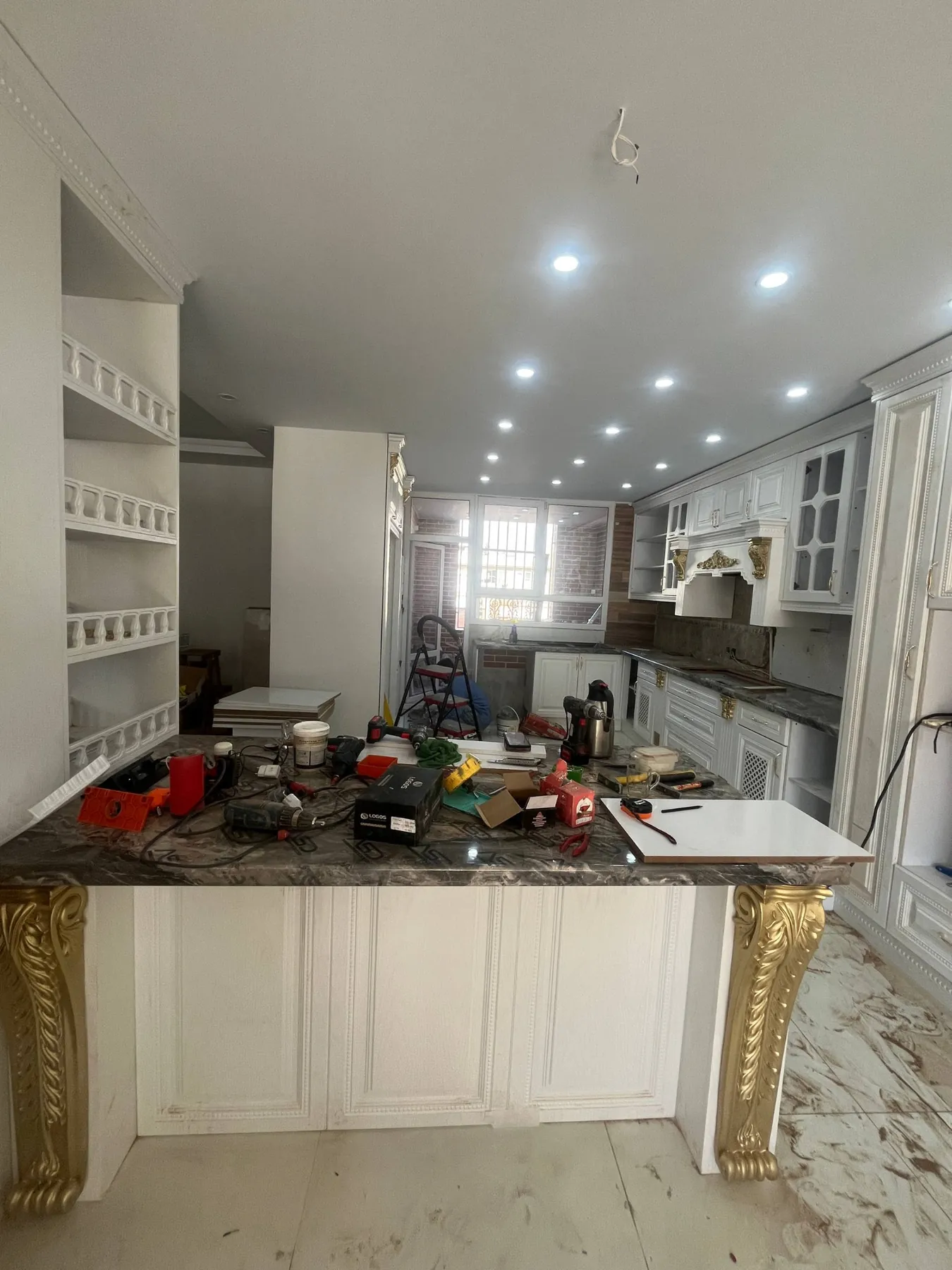The peninsula covered with installation tools and white ornate membrane cabinetry around the space